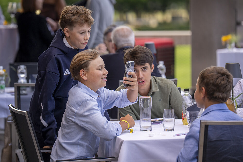 Vier Jungs an einem Tisch. Einer macht ein Foto. Zwei schauen ihm aufgeregt in die Kamera währen der letzte gegenüber in die Kamera lächelt. 