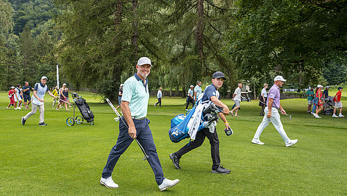 Sieger Mark Brown und sein Caddy laufen über den Golfplatz. Er ist in blau gekleidet mit weissem Cap. Hinter ihnen her laufen einige Zuschauer. Er lächelt in die Kamera und wirkt fröhlich.