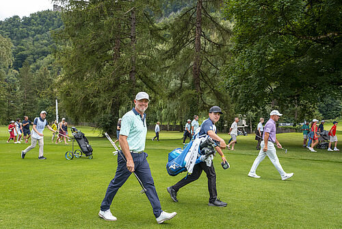 Sieger Mark Brown und sein Caddy laufen über den Golfplatz. Er ist in blau gekleidet mit weissem Cap. Hinter ihnen her laufen einige Zuschauer. Er lächelt in die Kamera und wirkt fröhlich.
