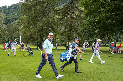Sieger Mark Brown und sein Caddy laufen über den Golfplatz. Er ist in blau gekleidet mit weissem Cap. Hinter ihnen her laufen einige Zuschauer. Er lächelt in die Kamera und wirkt fröhlich.