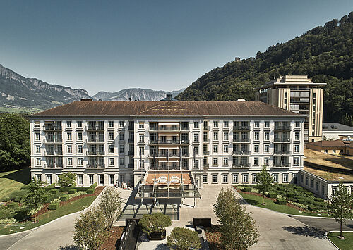 Luftaufnahme eines grossen Hotels mit einer modernen Fassade, umgeben von üppigem Grün und Bergen, die eine ruhige und einladende Atmosphäre vermitteln.