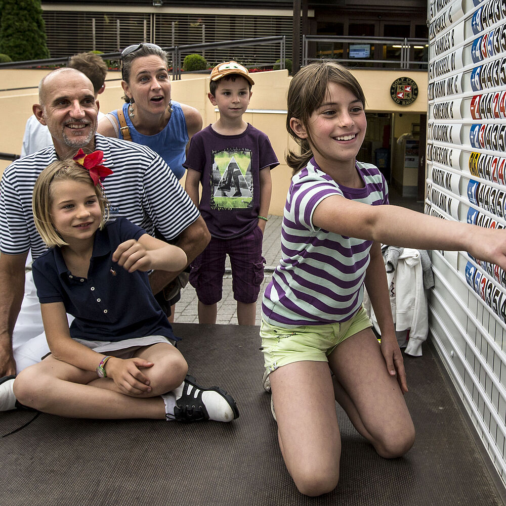 Zwei Erwachsene und drei Kinder, lächeln aufgeregt auf das Leaderboard. André Bossert, einer der Erwachsenen, erklärt den Kinds das System. Die Umgebung ist hell und im Freien.