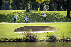 Golfer stehen auf dem Green. Vor ihnen im Bild ein Sandpunker und der Giessensee. 
