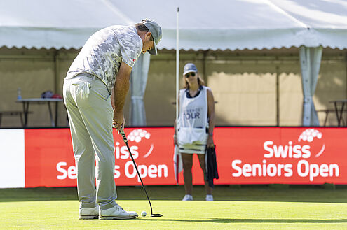 Keith Horne beim Putt auf Green 18. Er ist hell gekleidet und hinter ihm ist die LED Bande zu sehen die rot aufscheint.