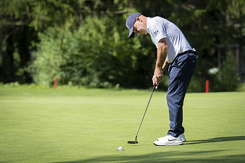 Robert Coles beim Putt auf dem Green. Im Hintergrund sieht man ein Gebüsch und rote Markierungen. Er trägt blau.