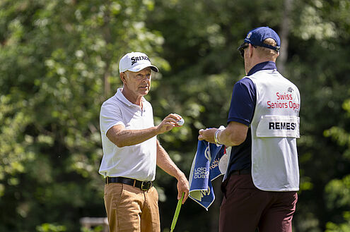 Jean-Francois Remesy und sein Caddy tauschen Golfbälle aus. Er trägt eine baige Hose und ein weisses Shirt mit weissem Cap. Sein Caddy steht ihm gegenüber und trägt dunkle Kleidung und einen weissen Bipp.